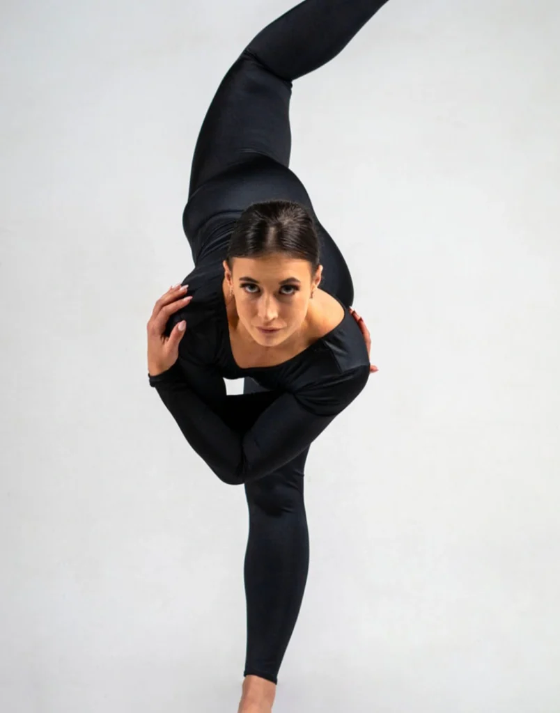Dancer balancing in a flexible pose while wearing a fitted black unitard.